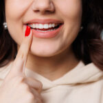 Happy girl showing toothy smile, pointing finger at healthy white teeth. Clinic patient satisfied with dentist service, enamel cleaning, whitening, dental care, correction