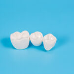 Plastic dental crowns, imitation of a dental prosthesis of a dental bridge for three teeth on a blue background.